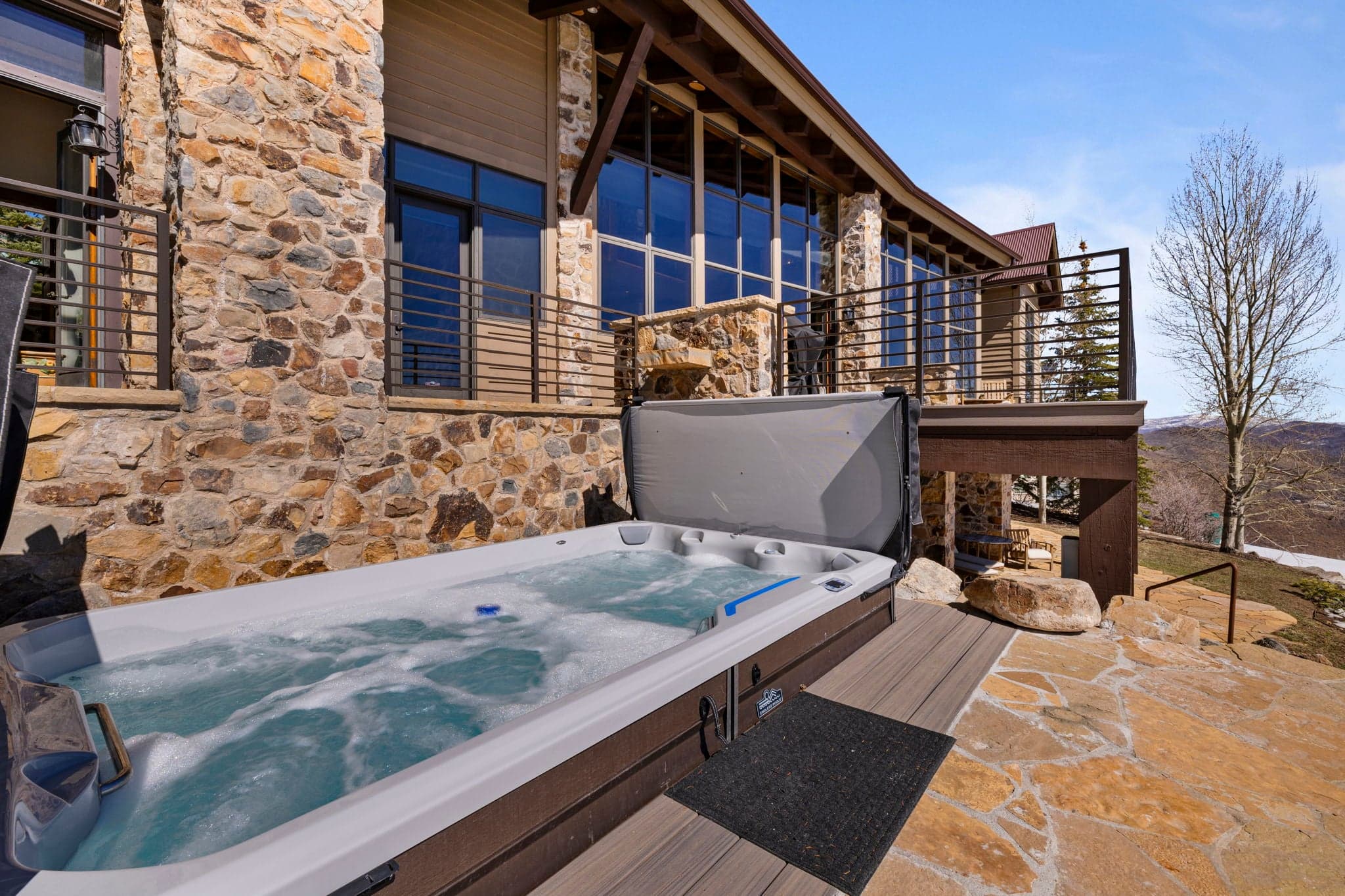 Outdoor hot tub on stone patio beside a mountain vacation home.