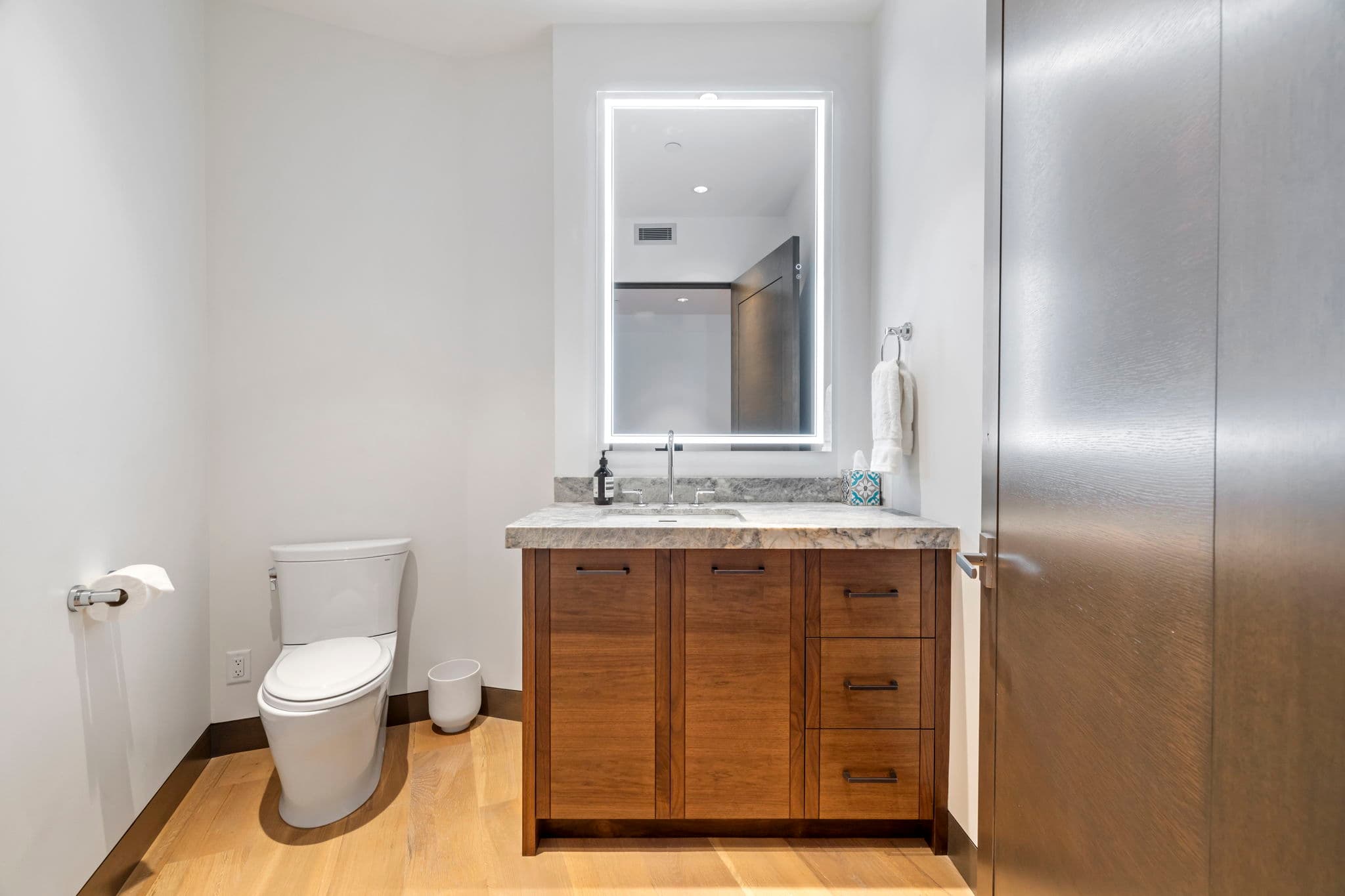 A guest bathroom with a toilet, a sink, and a mirror.